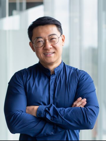 Portrait of successful mature boss, senior businessman in glasses Asian looking at camera and smiling, man with crossed arms working inside modern office building.